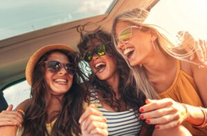 Three young women in the back of a car with windblown hair smiling