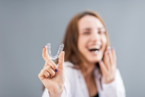 Woman laughing in background while holding Invisalign tray in foreground